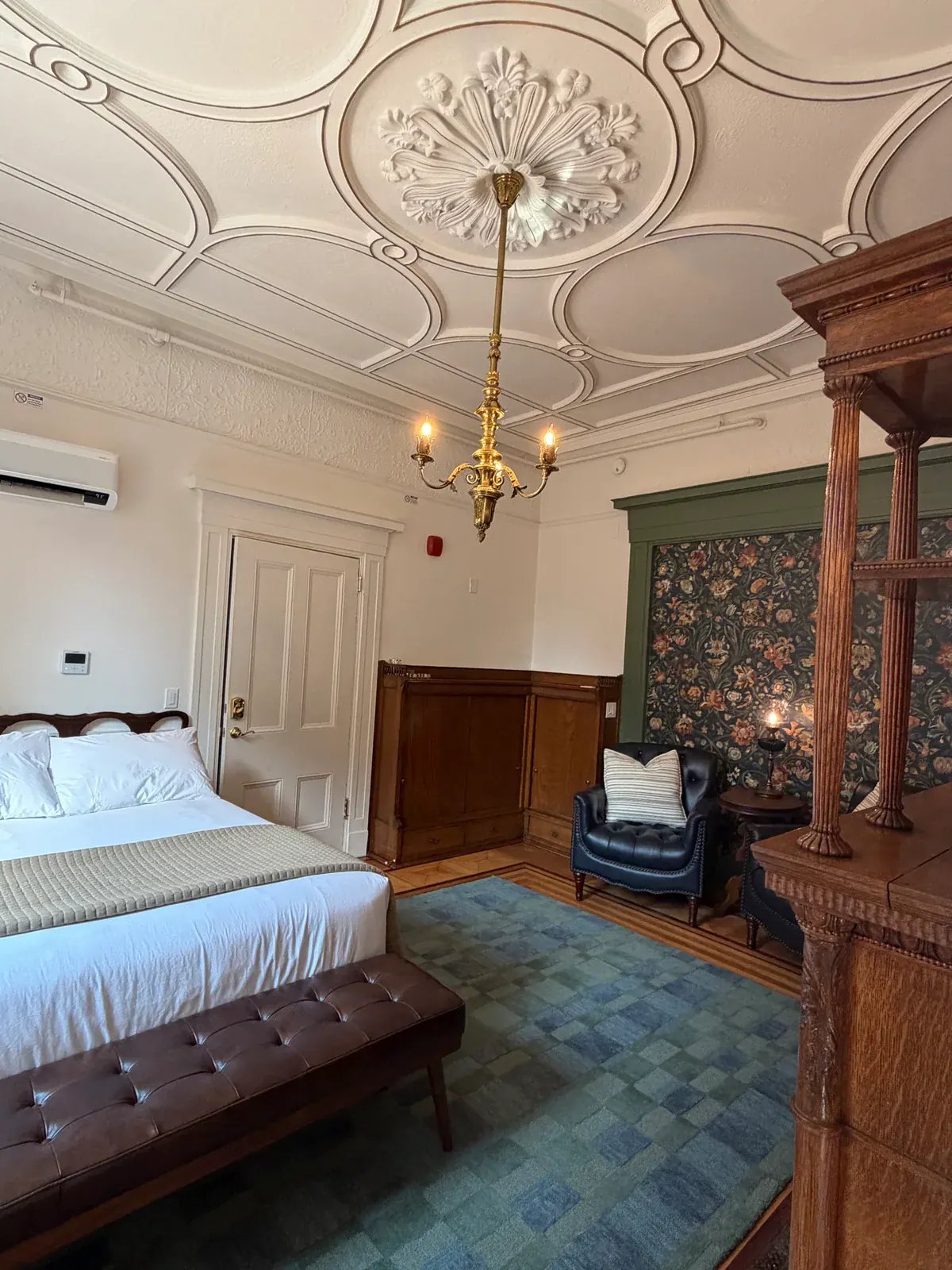 Ornate plasterwork and a brass chandelier above a Delphian guest room