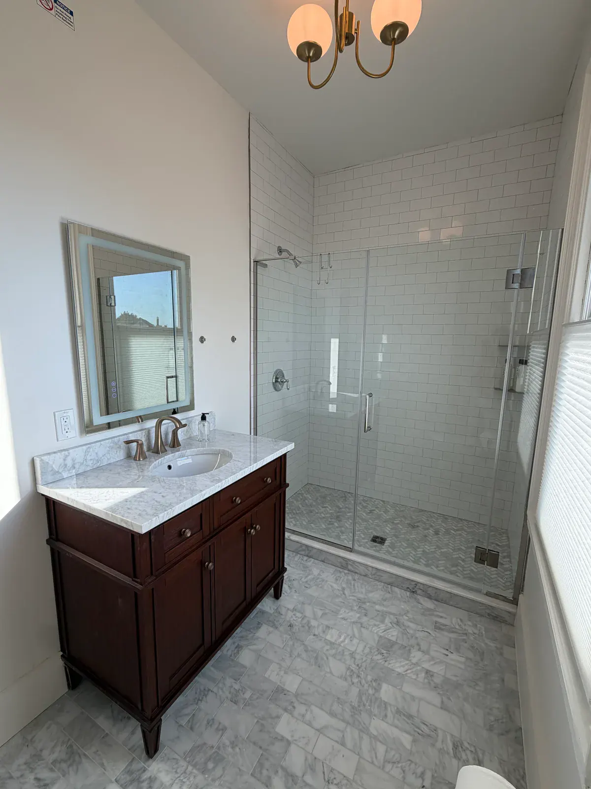 A Delphian ensuite bathroom with marble tile, a wood vanity, and a frameless glass shower
