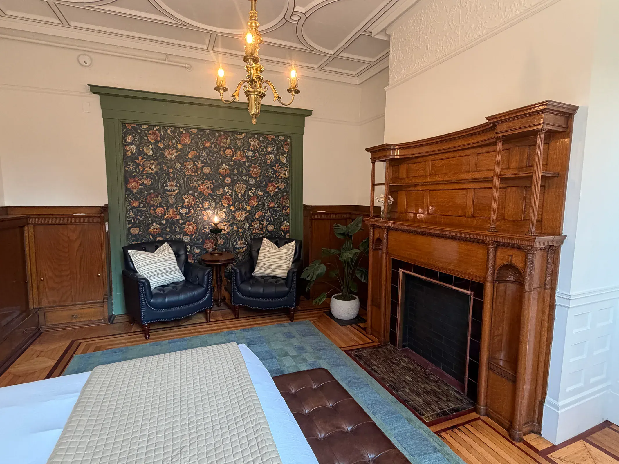 A Delphian guest room with carved woodwork, floral wall covering, leather chairs, and a historic fireplace