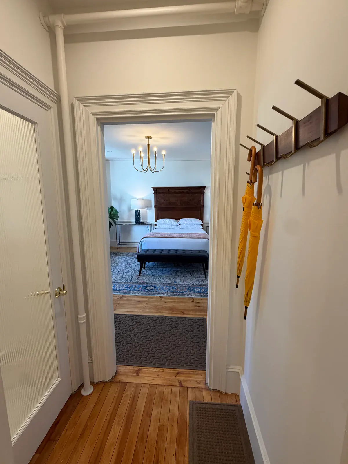 The hardwood entry passage to a Delphian guest room, with a bed visible beyond