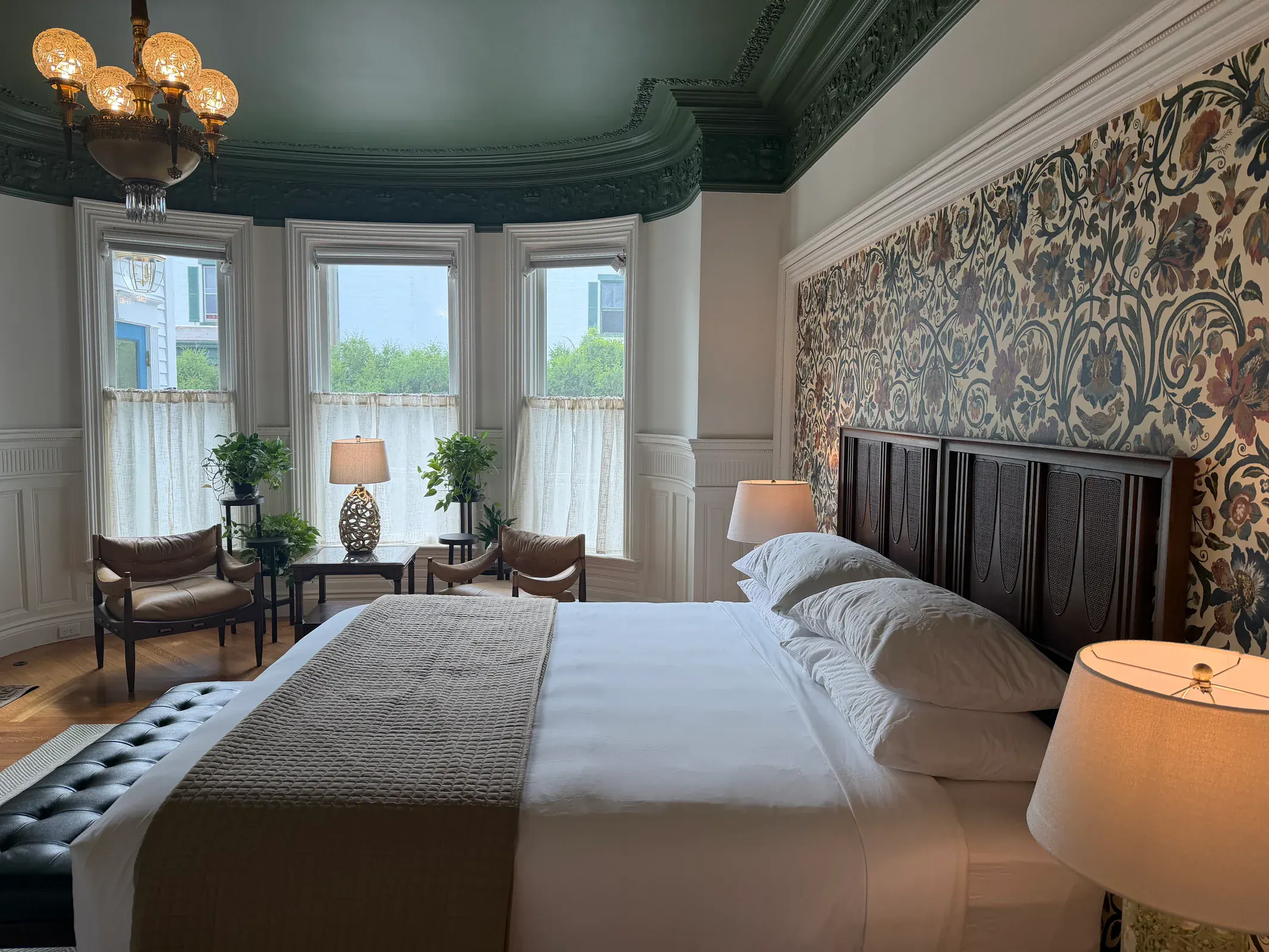 A Delphian guest room with a bed, patterned walls, a fireplace, and a bay-window seating area